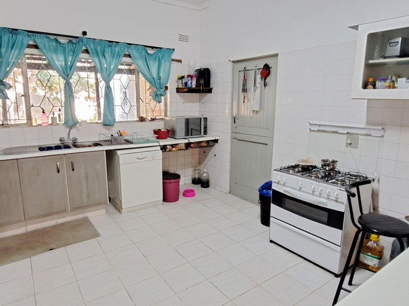 A functional kitchen featuring tiled flooring, white wall tiles, built-in cabinetry, a gas stove, and a double sink with a window view.