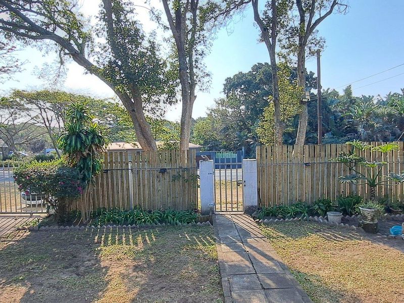 A view of the property's front garden area featuring a paved walkway, timber perimeter fencing, and mature trees.