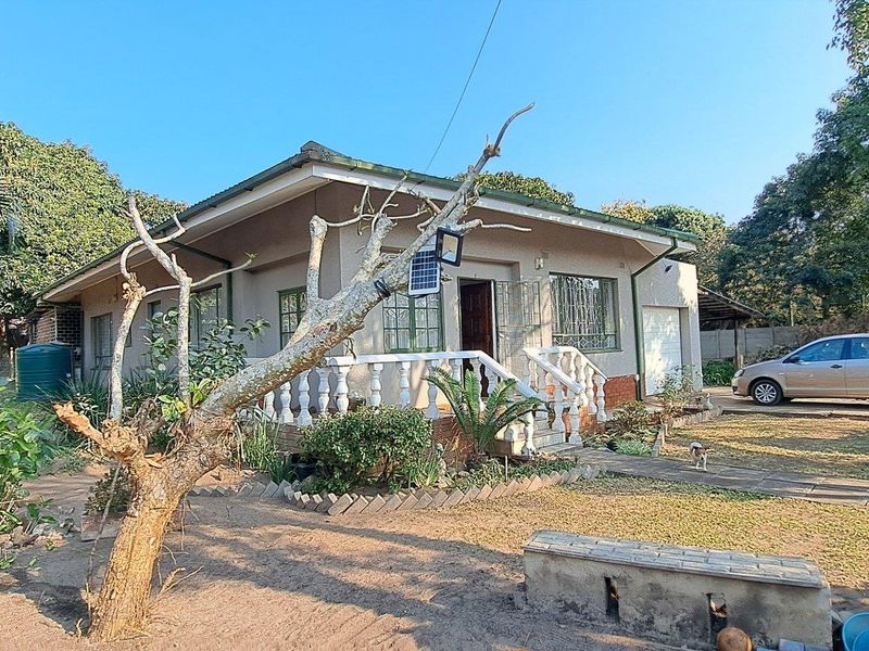 A single-story residential house featuring a front porch with balustrades, a paved driveway, and a surrounding garden area.