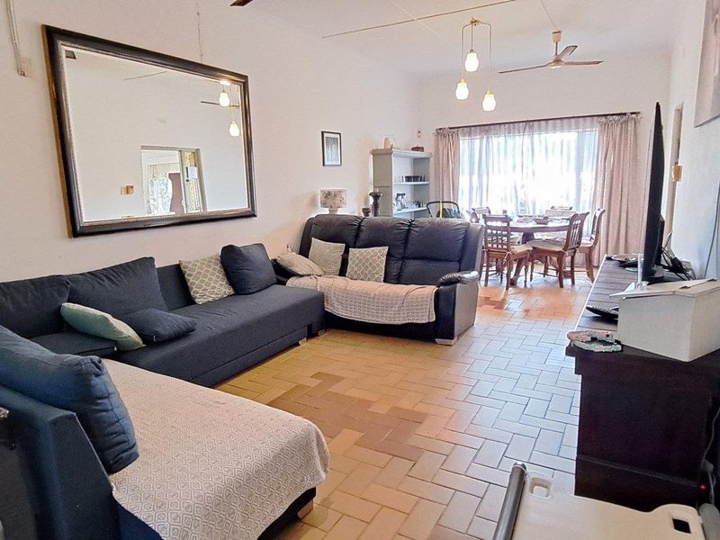 An open-plan living and dining area featuring tiled flooring, ceiling fans, and large windows allowing natural light into the space.
