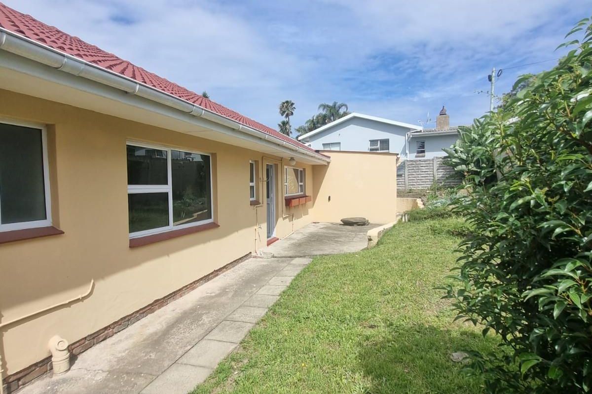 Rear exterior view of the house featuring a concrete patio area, lawn, and established garden borders.