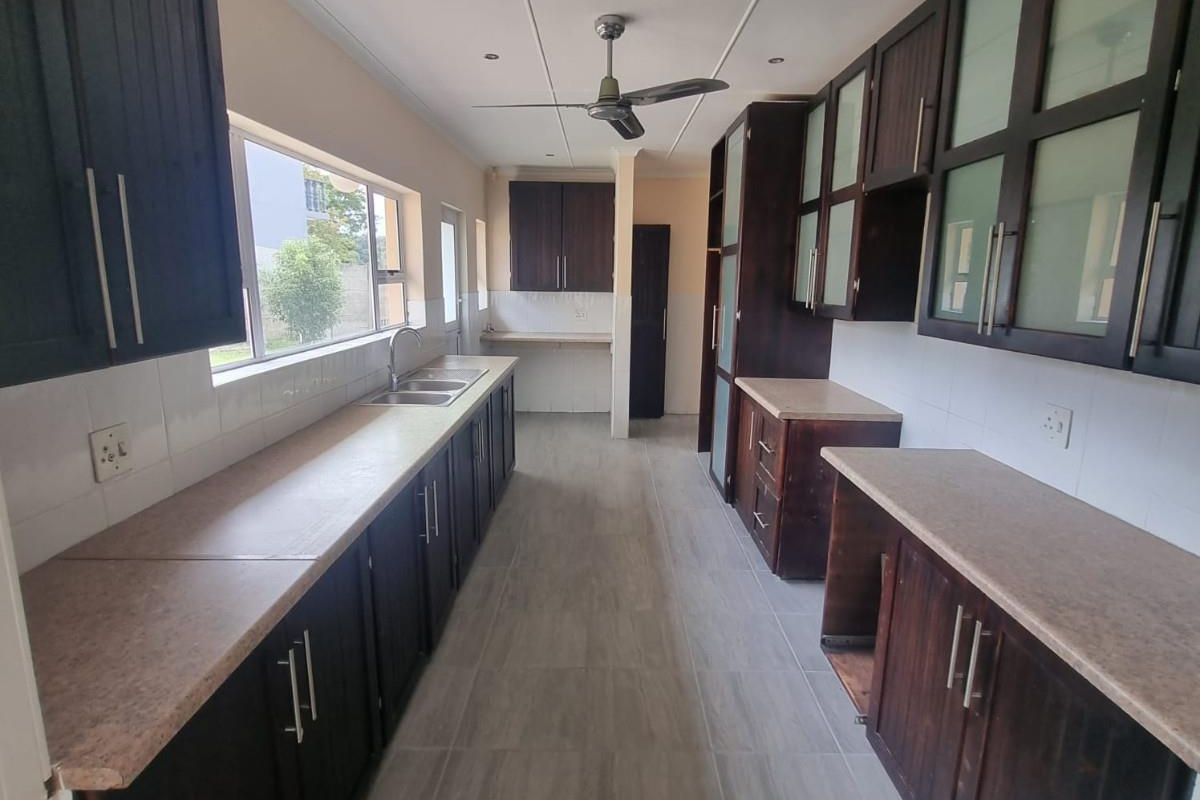 A galley-style kitchen featuring dark wood cabinetry, stone-look laminate countertops, tiled flooring, and a ceiling fan.