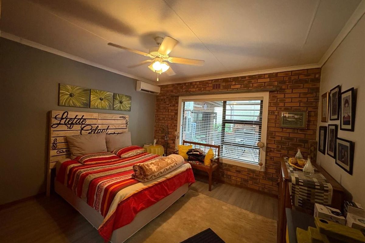 A cozy bedroom featuring a prominent exposed brick feature wall, ceiling fan, and wall-mounted air conditioning unit.