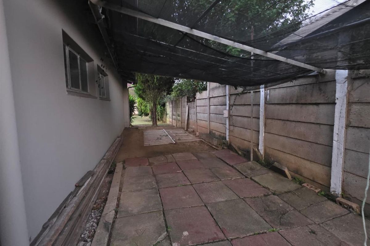 A side exterior area featuring paved flooring, a shade cloth canopy, and a concrete boundary wall.