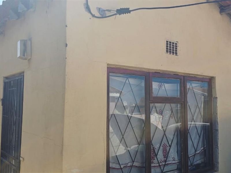 Exterior view of the property facade featuring tiled roofing, security-barred windows, and a side entrance door.