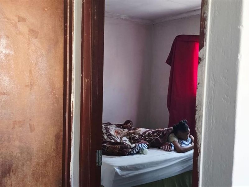 A view into a bedroom featuring a doorway with a worn wooden door and frame, leading to a basic sleeping area.