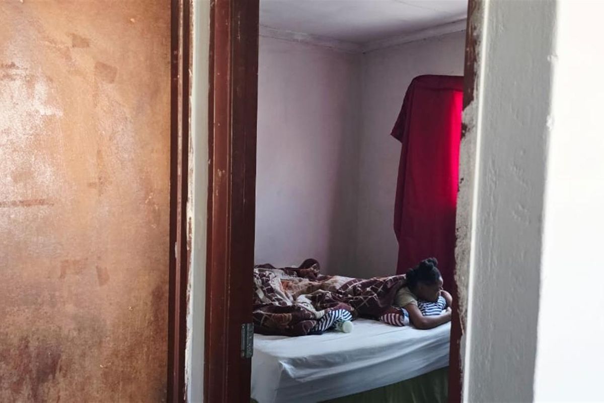 A view into a bedroom featuring a doorway with a worn wooden door and frame, leading to a basic sleeping area.