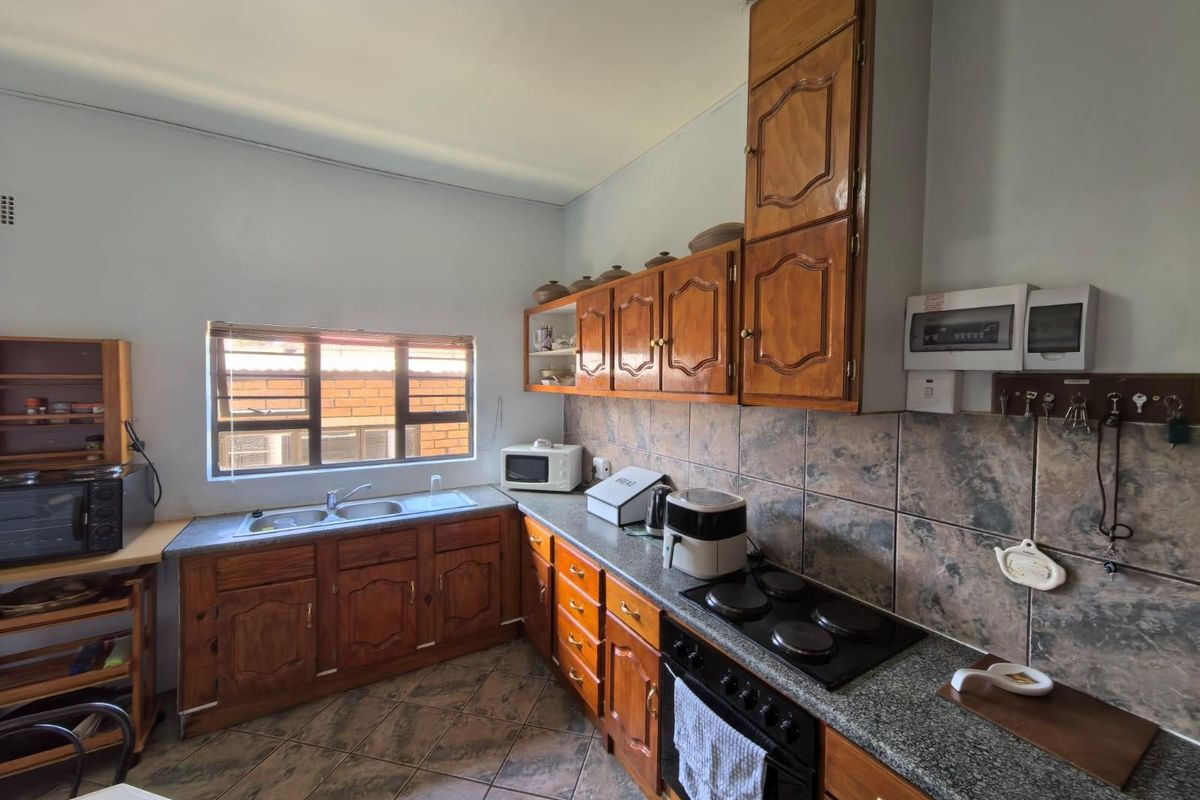 A functional kitchen featuring traditional wooden cabinetry, granite-look countertops, a built-in electric hob and oven, and a double-basin sink with tiled backsplash.