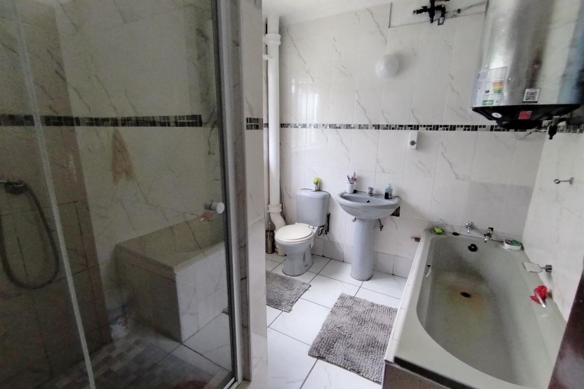 A bathroom featuring a glass-enclosed shower, a pedestal sink, a toilet, and a bathtub with visible wear and exposed plumbing fixtures.
