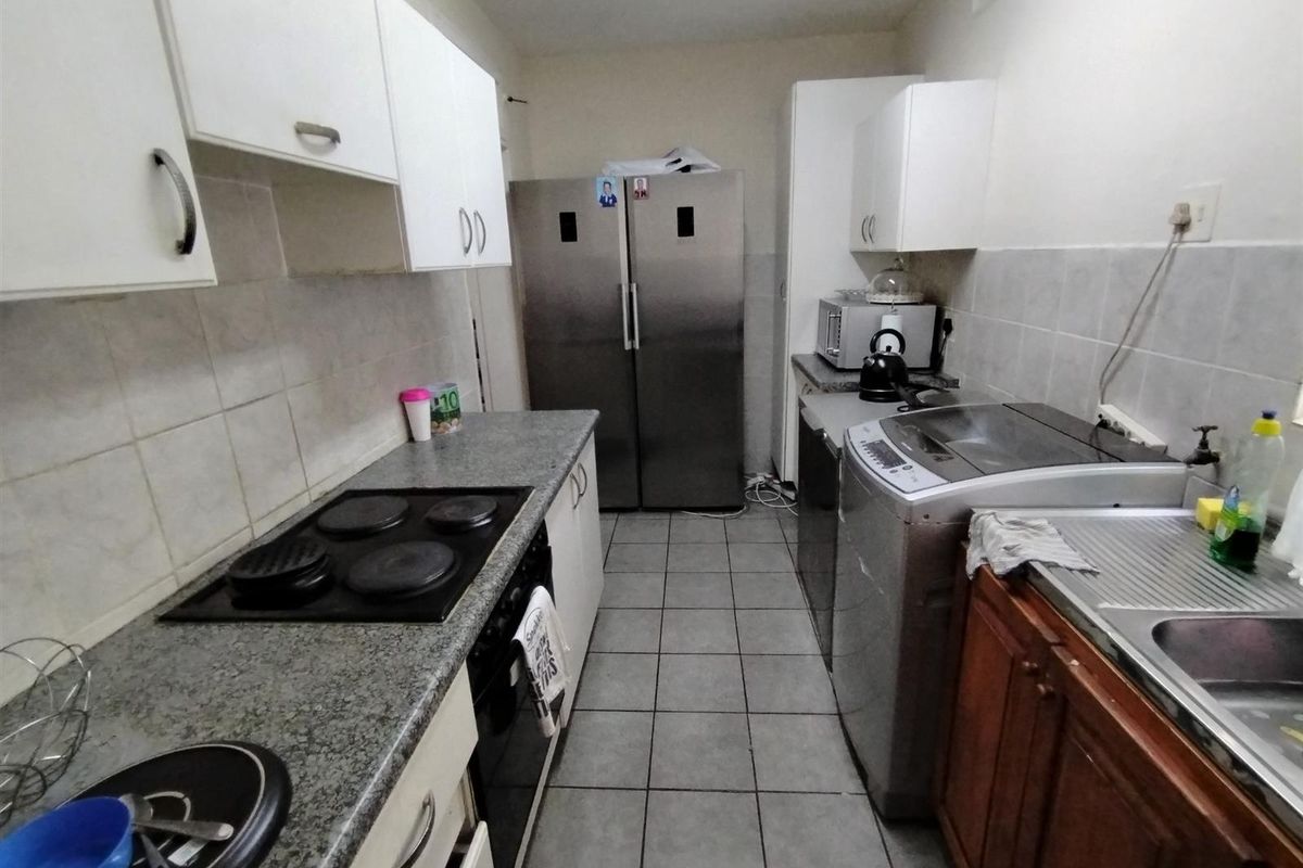 A functional galley-style kitchen featuring granite countertops, a built-in electric hob, oven, and tiled flooring with ample storage cabinetry.
