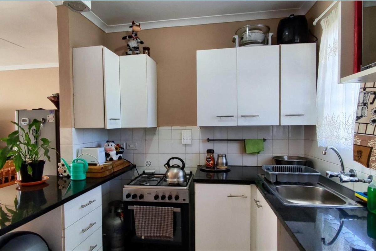 Compact kitchen featuring white cabinetry, black countertops, a gas stove, and a stainless steel sink with a tiled splashback.