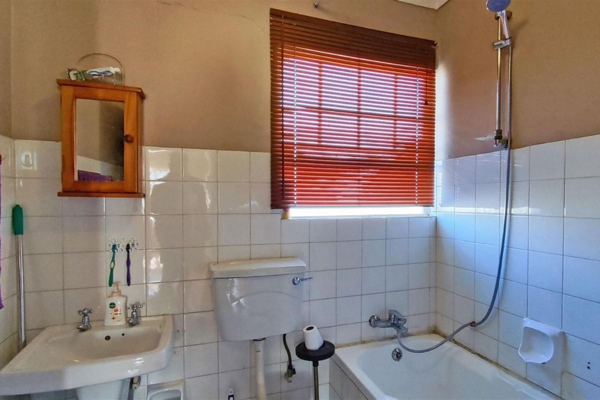 A dated bathroom featuring a standard bathtub with shower attachment, a wall-mounted basin, and a low-level flush toilet with tiled walls.