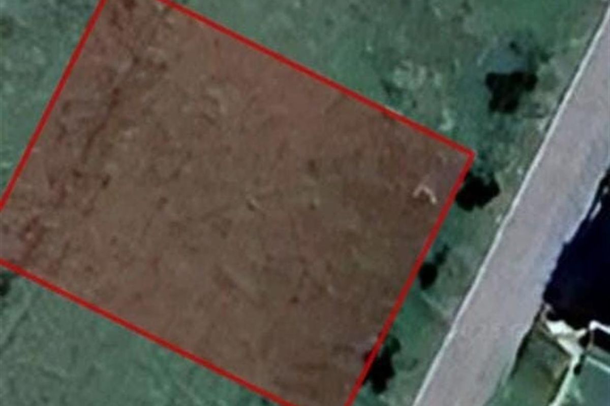 An aerial satellite view of a vacant residential land plot with a red boundary overlay indicating the property lines.