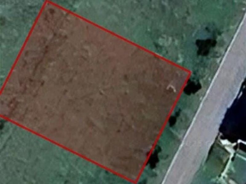 An aerial satellite view of a vacant residential land plot with a red boundary overlay indicating the property lines.