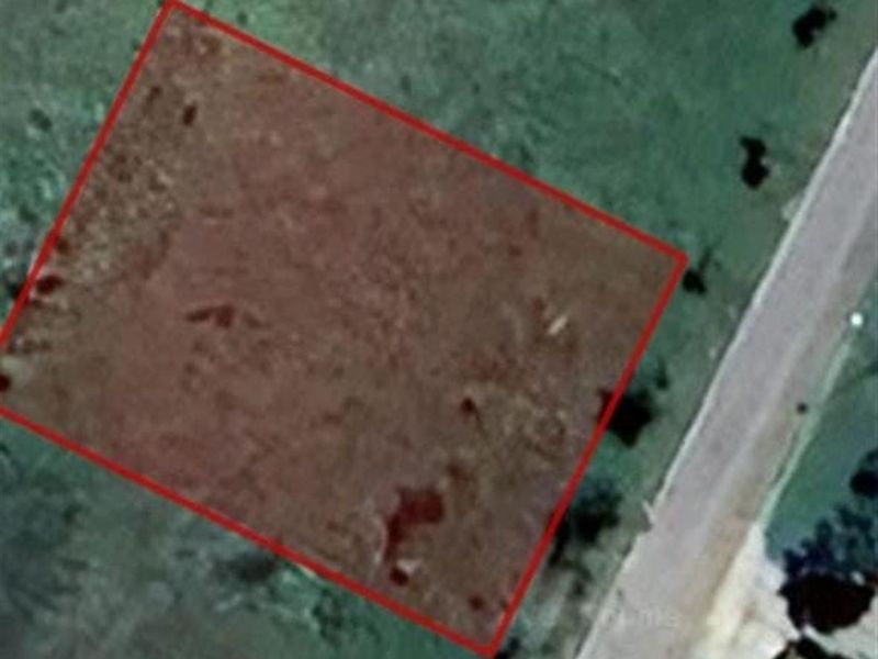 An aerial view of a vacant residential plot with a red boundary overlay indicating the property lines.