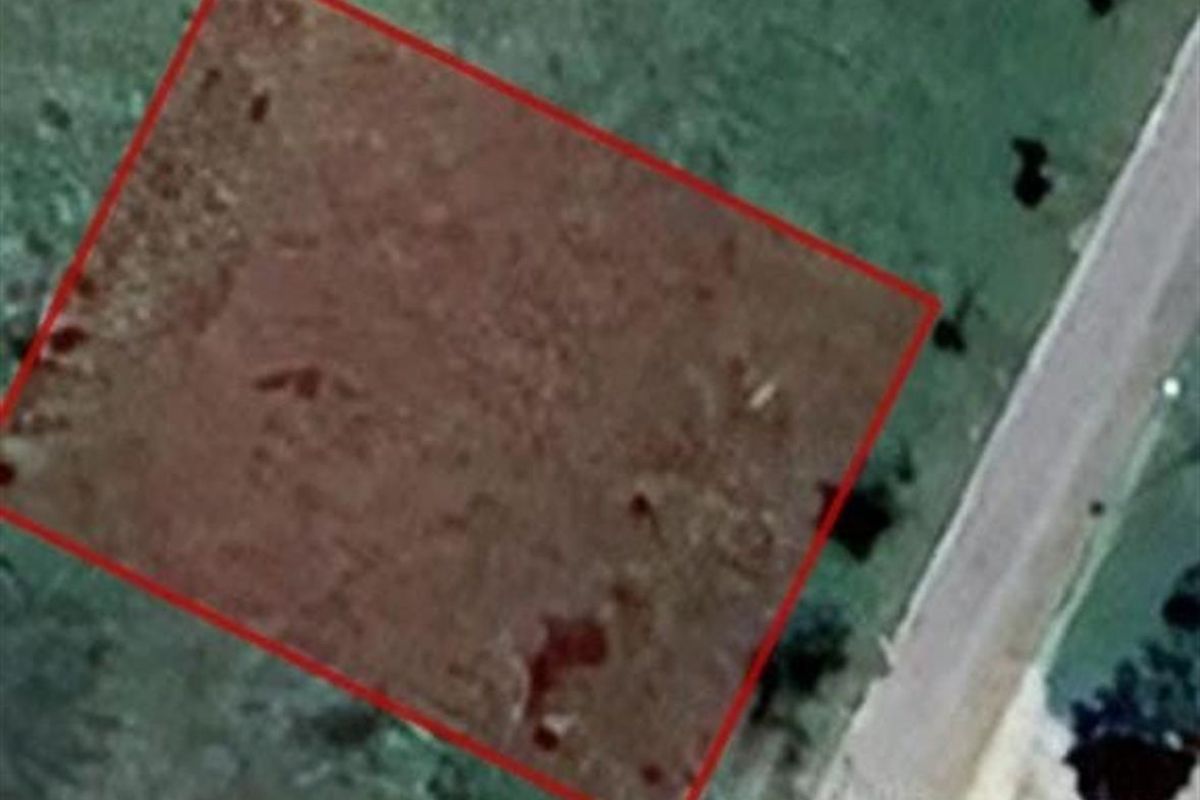An aerial view of a vacant residential plot with a red boundary overlay indicating the property lines.