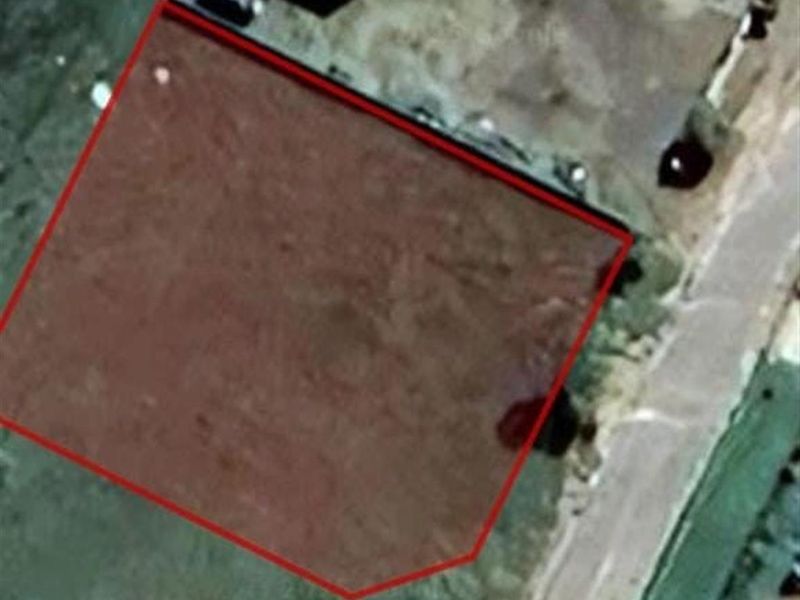 An aerial view of a vacant residential plot with property boundaries highlighted in red.