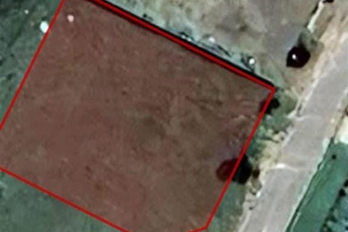 An aerial view of a vacant residential plot with property boundaries highlighted in red.