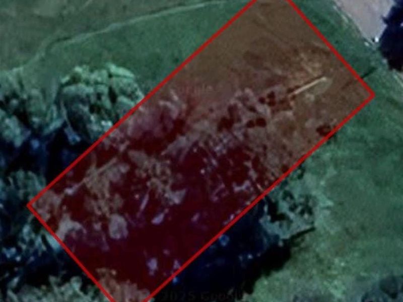 An aerial view of a vacant residential plot of land, highlighted with a red boundary overlay.