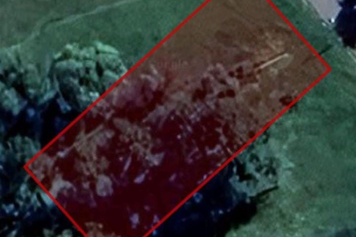 An aerial view of a vacant residential plot of land, highlighted with a red boundary overlay.