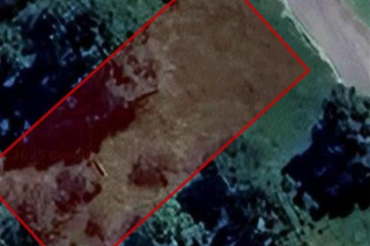 An aerial view of a vacant residential plot of land, outlined in red, showing the natural terrain and surrounding vegetation.