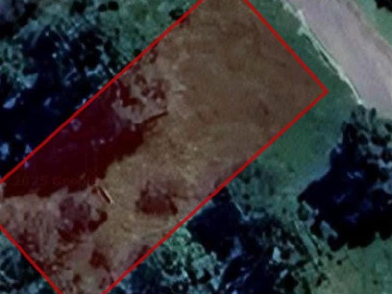 An aerial view of a vacant residential plot of land, outlined in red, showing the natural terrain and surrounding vegetation.