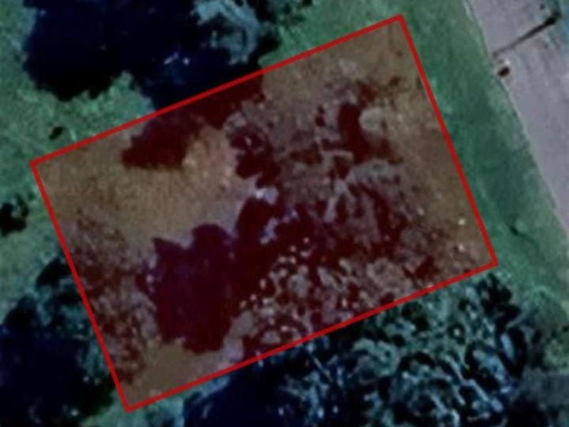 An aerial satellite view of a vacant residential plot outlined in red, showing the land's position relative to the surrounding area.