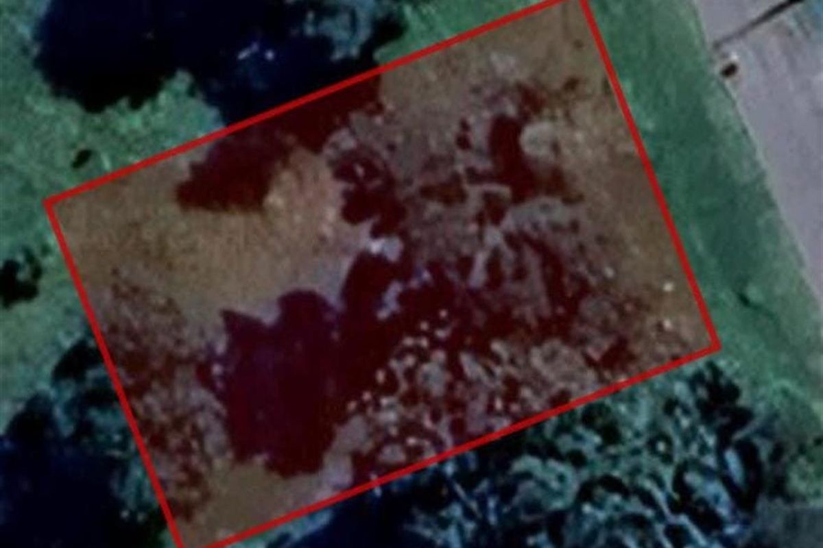 An aerial satellite view of a vacant residential plot outlined in red, showing the land's position relative to the surrounding area.