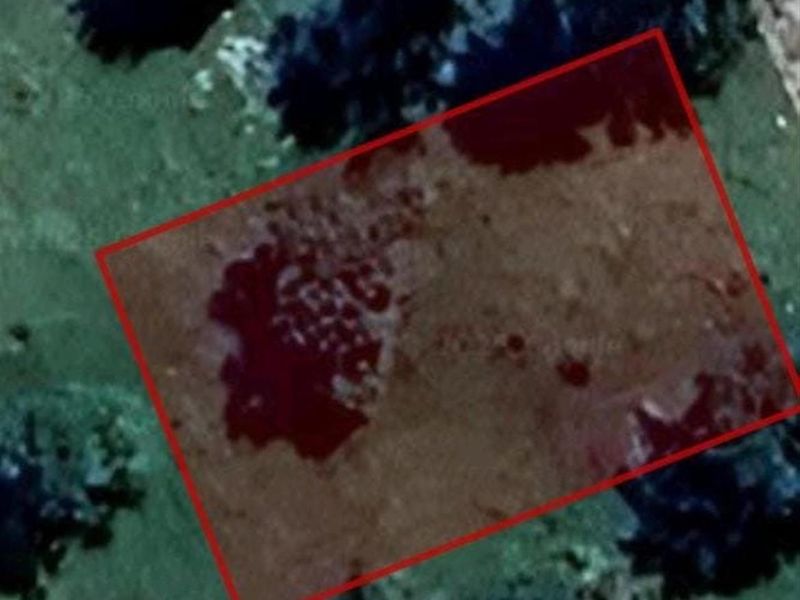 An aerial view of a vacant residential plot outlined in red, showing natural terrain and surrounding vegetation.
