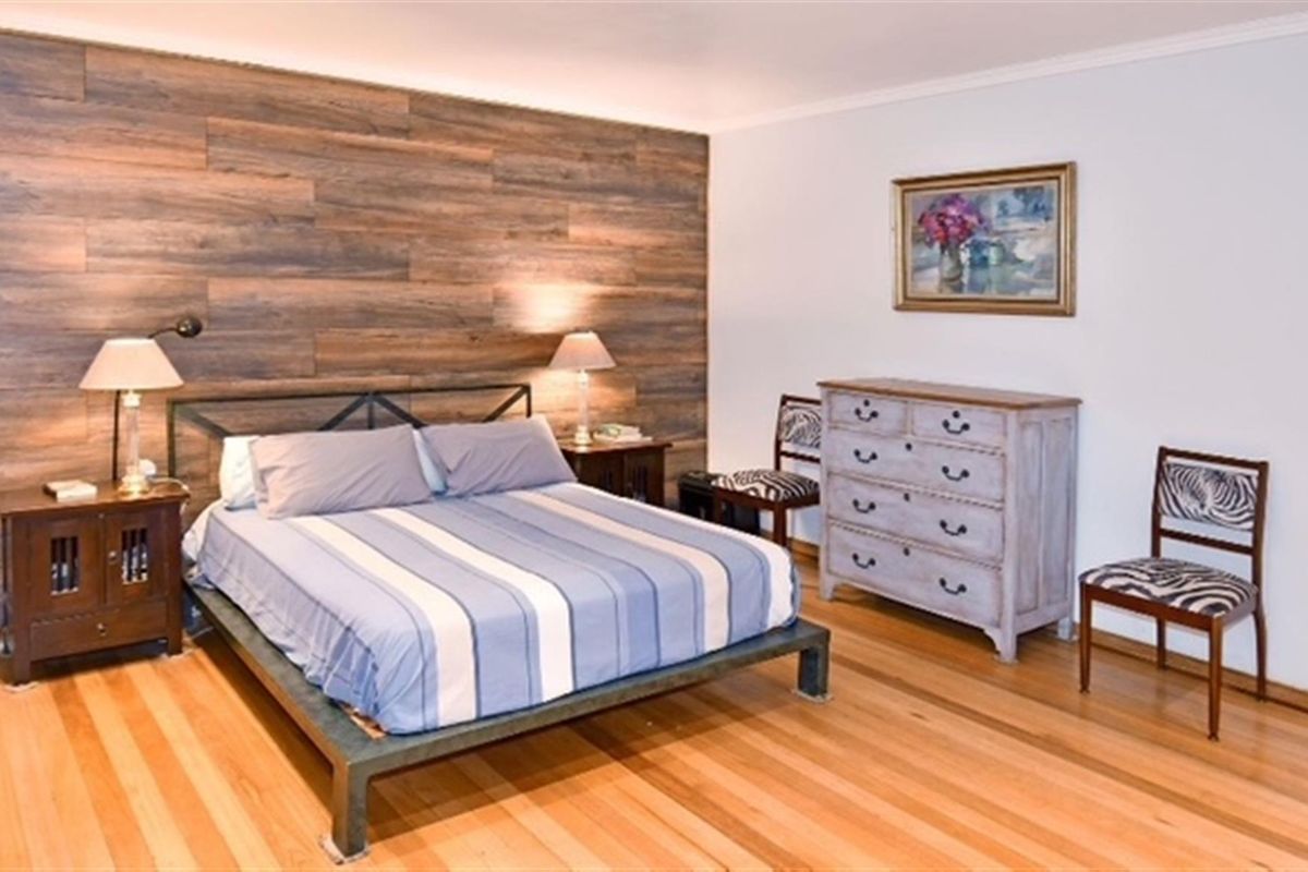 A well-maintained bedroom featuring polished timber flooring and a prominent wood-look feature wall.