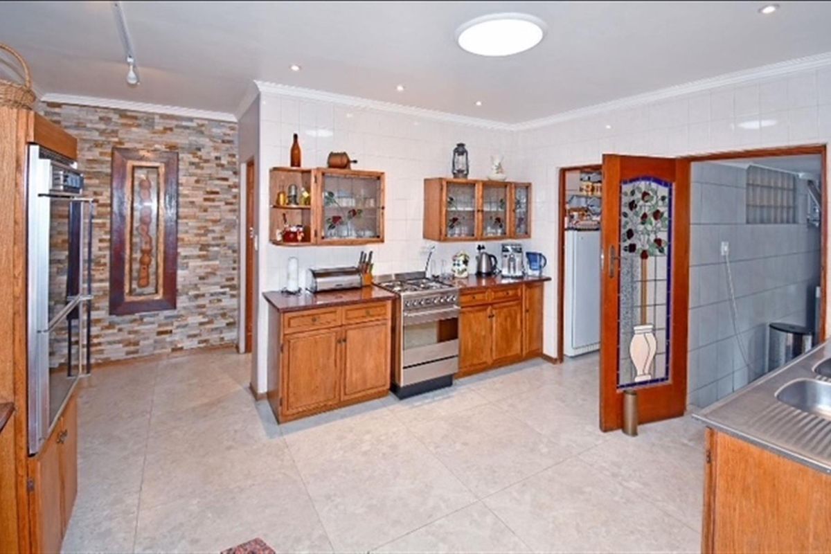 Spacious kitchen featuring wooden cabinetry, a gas stove, tiled flooring, and a decorative stone feature wall, with an adjacent pantry area.