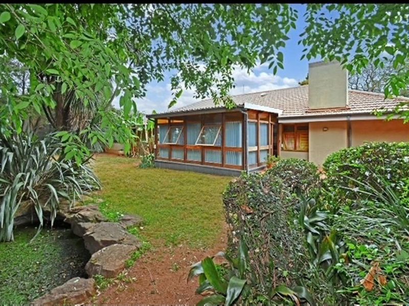 Rear view of the house featuring a tiled roof, chimney, and an enclosed patio area overlooking a landscaped garden with a rock feature.