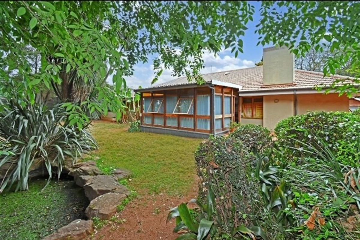Rear view of the house featuring a tiled roof, chimney, and an enclosed patio area overlooking a landscaped garden with a rock feature.