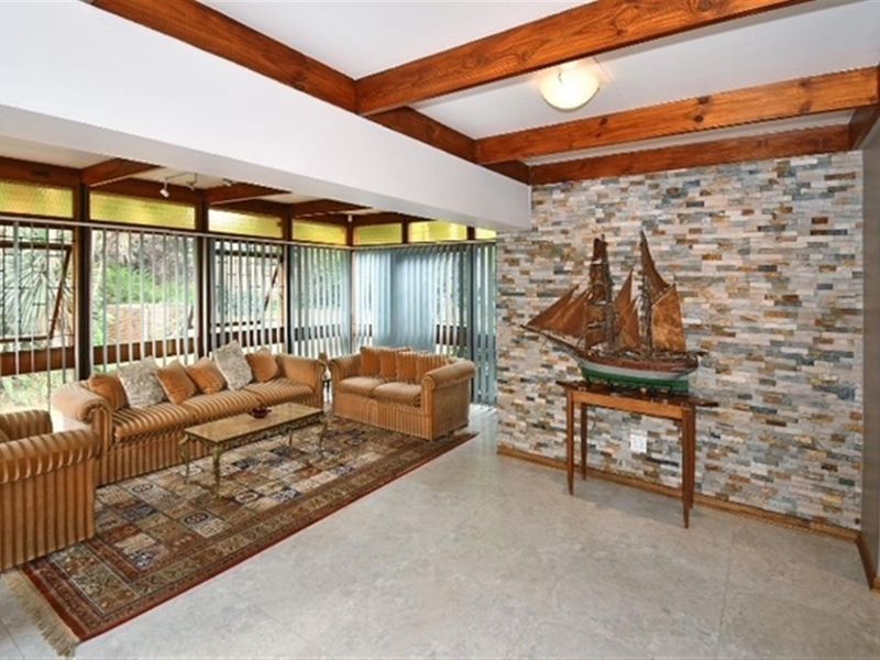 Spacious living room featuring a striking stone feature wall, exposed timber ceiling beams, and large windows that provide ample natural light.