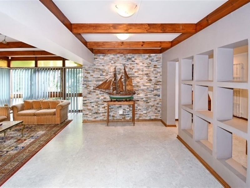 Spacious living area featuring exposed timber ceiling beams, a decorative stone feature wall, and unique built-in wall niches with tiled flooring throughout.