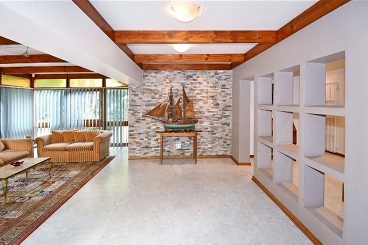 Spacious living area featuring exposed timber ceiling beams, a decorative stone feature wall, and unique built-in wall niches with tiled flooring throughout.