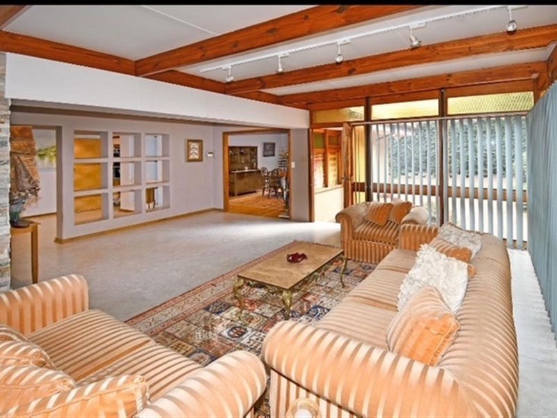 Spacious living room featuring exposed timber ceiling beams, a stone feature wall, and large glass doors providing ample natural light.