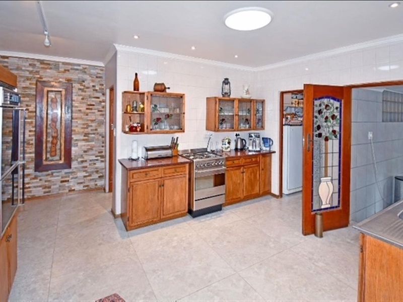Spacious kitchen featuring wooden cabinetry, a gas stove, stone veneer accent wall, and a unique stained glass door leading to a pantry area.