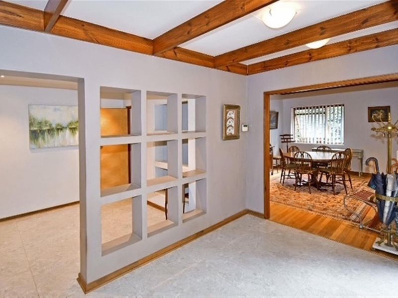 Living area featuring exposed timber ceiling beams, a unique built-in decorative room divider, and a transition between tiled and timber flooring.