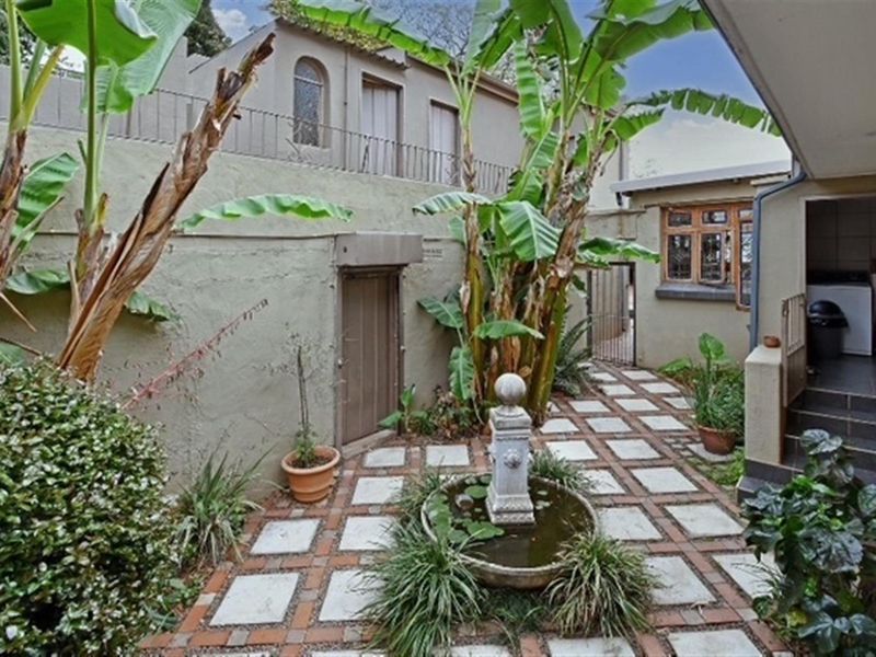 A private rear courtyard featuring a central water fountain, paved flooring, and established landscaping, enclosed by high boundary walls.