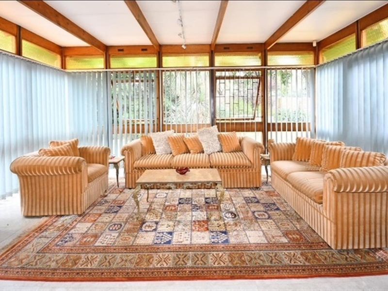 Spacious living area featuring exposed timber ceiling beams, extensive glass paneling, and tiled flooring, offering a bright and airy atmosphere.