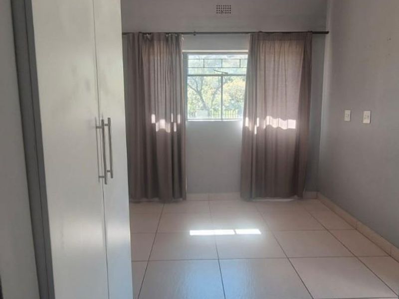 A bright, empty bedroom featuring neutral tiled flooring, built-in cupboards, and a functional ceiling light fixture.