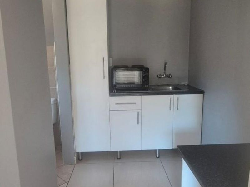 A compact scullery area featuring white built-in cabinetry, a stainless steel sink, and tiled flooring, providing functional prep and wash-up space.