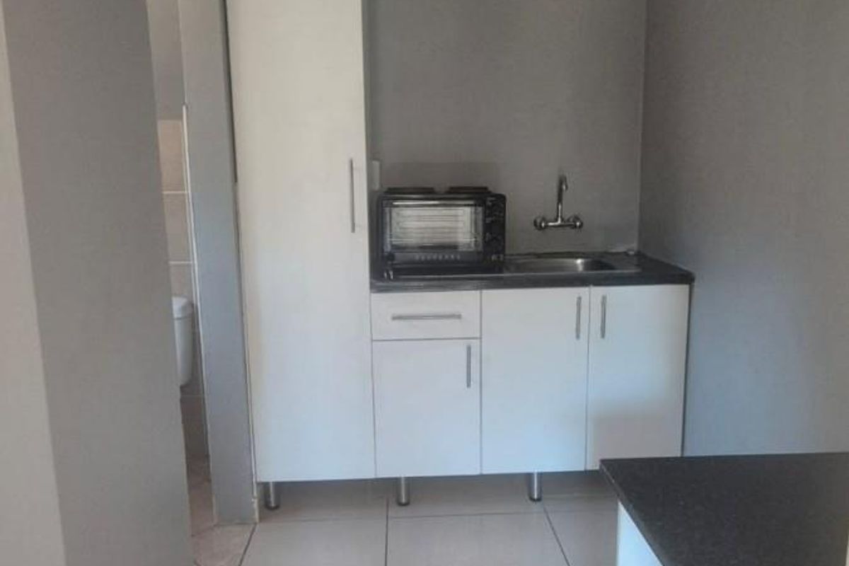 A compact scullery area featuring white built-in cabinetry, a stainless steel sink, and tiled flooring, providing functional prep and wash-up space.