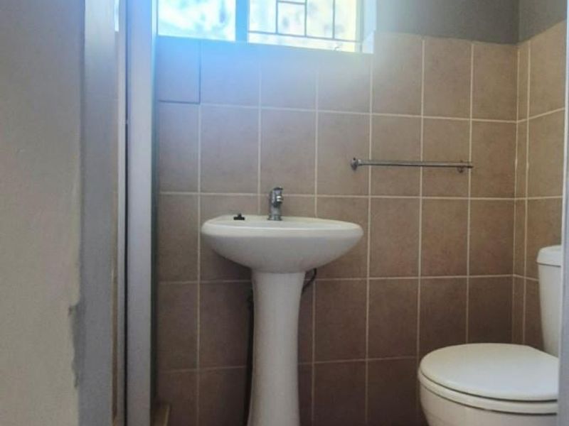 A functional bathroom featuring a pedestal basin, toilet, and neutral wall and floor tiling with a window for natural light.