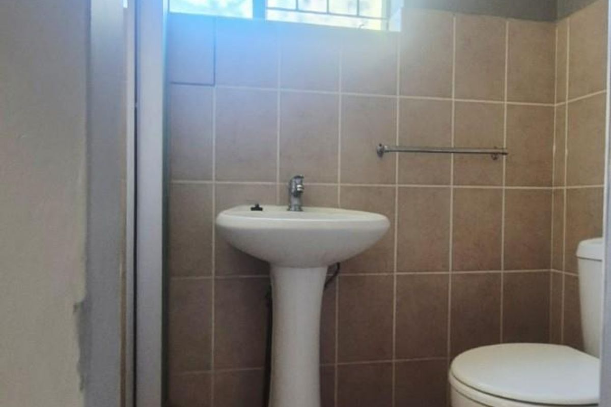 A functional bathroom featuring a pedestal basin, toilet, and neutral wall and floor tiling with a window for natural light.