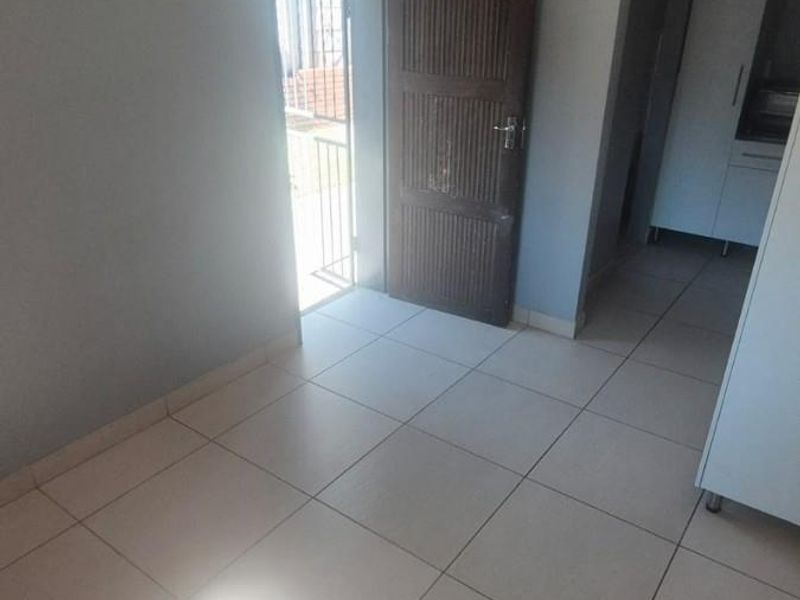 An empty entrance area featuring neutral tiled flooring, a wooden door, and access to an adjacent room with built-in cabinetry.
