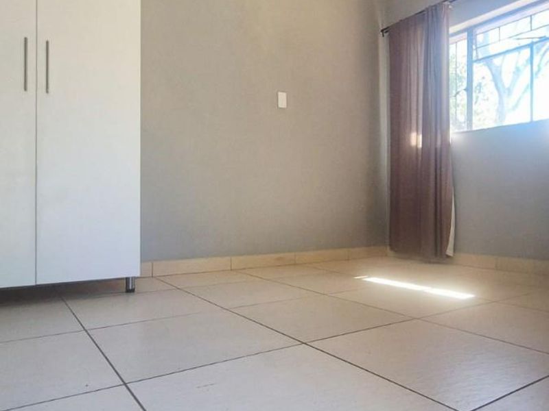A bright, empty bedroom featuring neutral tiled flooring, a built-in wardrobe, and a large window allowing for natural light.
