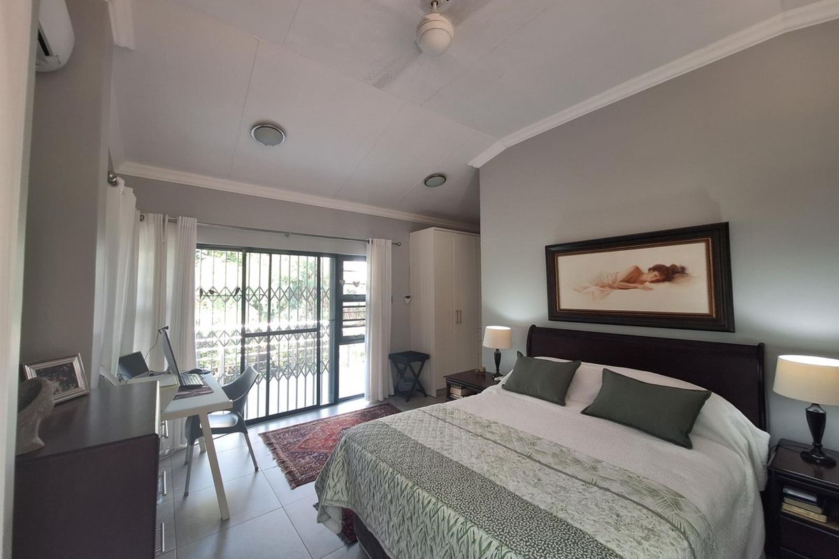 A well-maintained bedroom featuring tiled flooring, built-in cabinetry, a ceiling fan, and sliding glass doors with security gates leading to the exterior.
