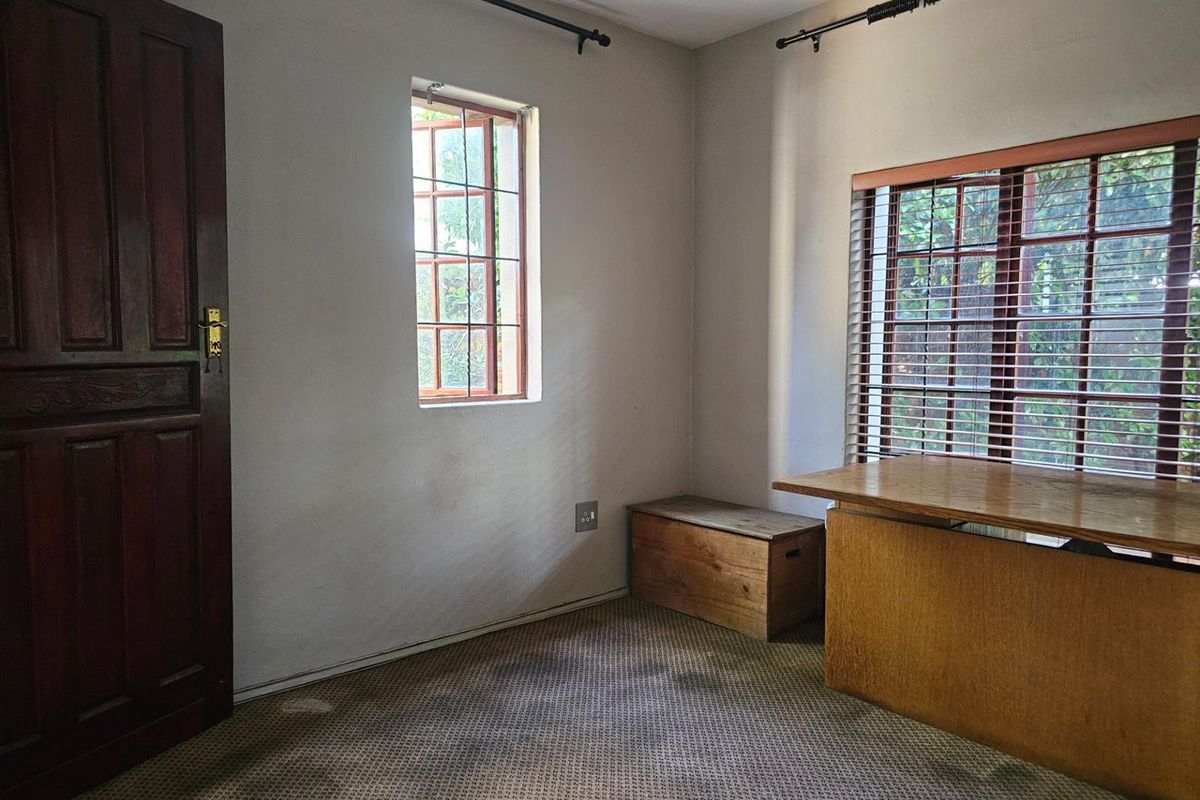 A bedroom featuring timber-framed windows, wooden door, and fitted carpet, offering a functional space with natural light.